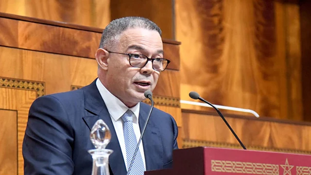 فوزي لقجع واقفًا بمنصة البرلمان يقدّم مشروع قانون المالية 2027
